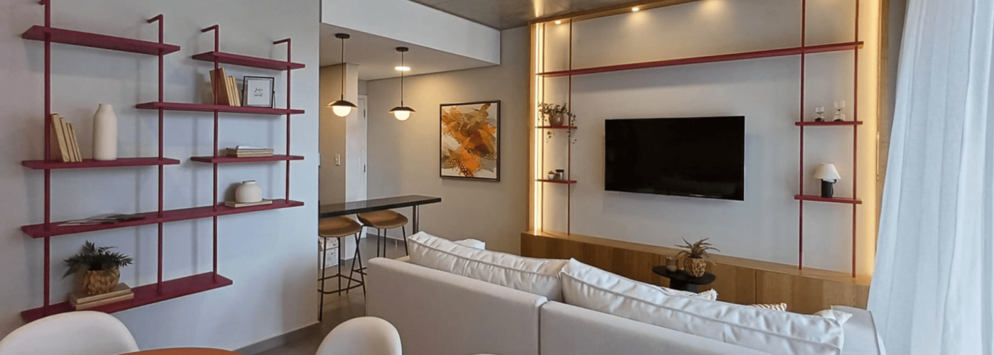 Salon moderne d’un appartement meublé à Asunción, au Paraguay, avec canapé blanc, télévision murale, cuisine ouverte et étagères décoratives..