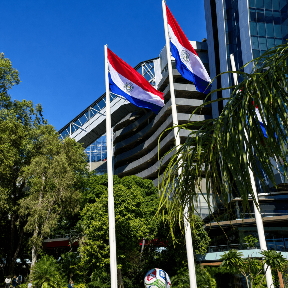 Drapeaux du Paraguay devant le complexe Paseo La Galería à Asunción, entouré de bâtiments modernes et de végétation.