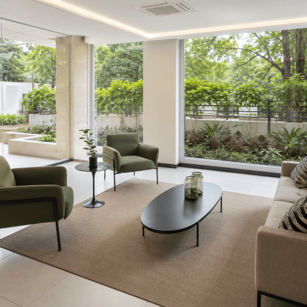 Salon moderne avec fauteuils verts, grandes baies vitrées et vue sur un jardin dans une résidence à Asunción, au Paraguay.